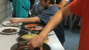 Children prepare desserts with various ingredients at the table.