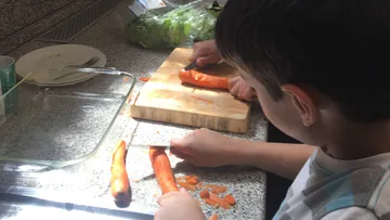 Carrots are cut by a child in the kitchen.