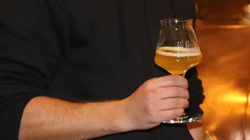 A man is holding a glass of light beer.
