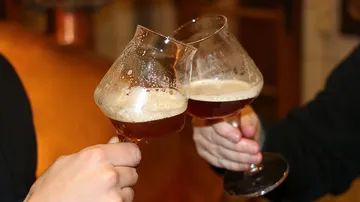 Zwei Biergläser stoßen in einem gemütlichen Raum an.