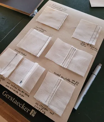 Stoffquadrate zeigen verschiedene Nähtechniken auf Holzplatte.