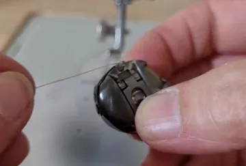 Faden wird durch eine Nähmaschinen-Nadel eingefädelt.