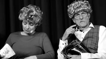 Two people sit on stage with shocked facial expressions.