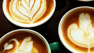 Kaffeetassen mit kunstvollen Milchschaum-Mustern auf einem Tisch.
