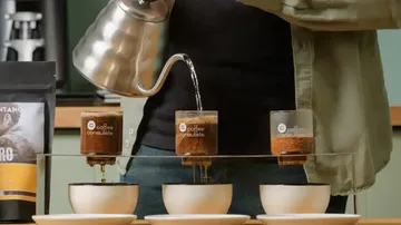 Coffee pot pours water into filters while drops of coffee fall.