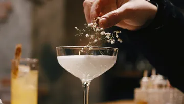Ein Cocktailglas wird mit weißen Blumen dekoriert.
