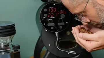 Mann riecht Kaffeebohnen vor einer Röstmaschine.