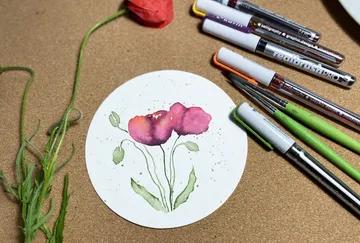 Watercolor flowers on paper, surrounded by art supplies and nature.