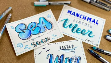 Drei Postkarten mit handgezeichneten Schriftzügen und Stiften.