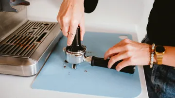 Hände drücken einen Kaffeepfanneneinsatz auf einer Fläche.