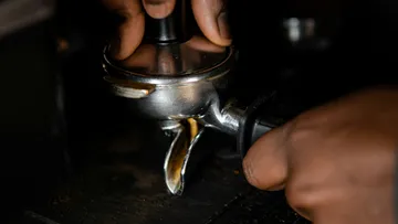 Eine Hand drückt einen Siebträger auf eine Espressomaschine.