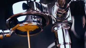 Espressomaschine gießt braune Flüssigkeit in Tasse.
