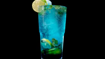 Blauer Cocktail mit Eis und Zitronenscheiben in einem Glas.