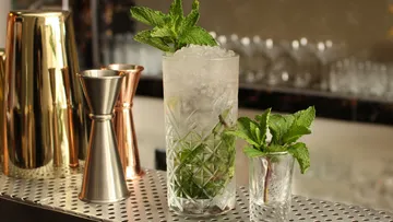 Glass with mint and ice is standing at a bar.