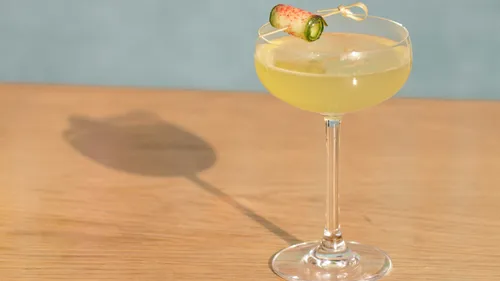 Cocktail im Glas, steht auf einem Holztisch, beleuchtet.