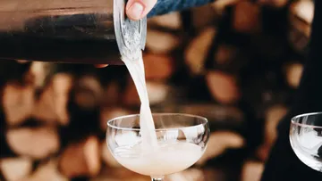Ein Cocktail wird in eine Schale gegossen, Holz im Hintergrund.