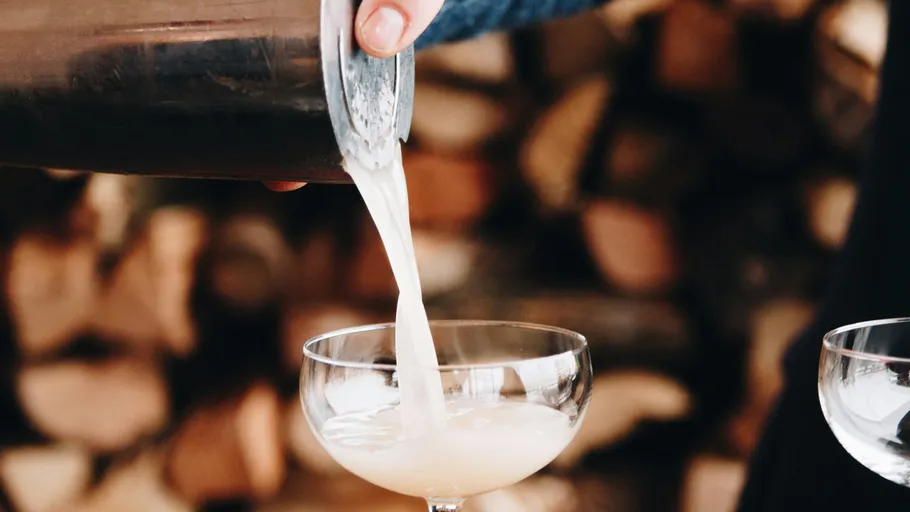 Ein Cocktail wird in eine Schale gegossen, Holz im Hintergrund.