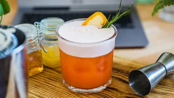 Ein Cocktail auf einem Holztisch neben einem Laptop.