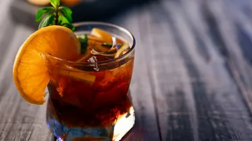 Cocktail glass with ice, orange slice and mint leaf on wood.