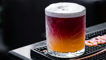 Colourful drink in a glass, frothy on top, in a bar.