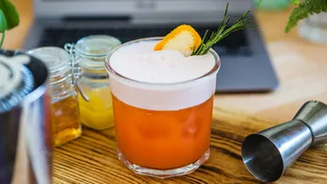 A cocktail is sitting on a wooden board next to a laptop.