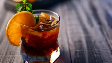 A glass with ice and an orange on a table.