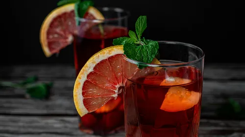 Zwei Gläser mit roten Getränken, garniert mit Früchten.