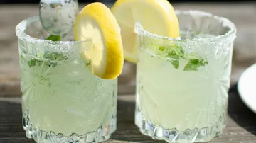 Zwei Gläser mit Mojito, serviert auf einem Holztisch.