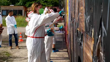 Menschen in Overalls sprayen Graffiti an ein Fahrzeug.