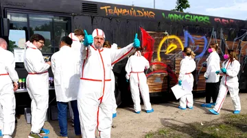 People wearing white overalls spray graffiti on a bus.