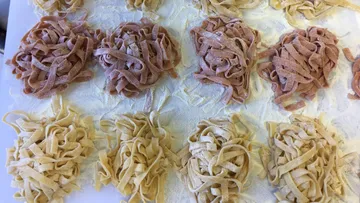 Homemade pasta nests lie on a floured table.