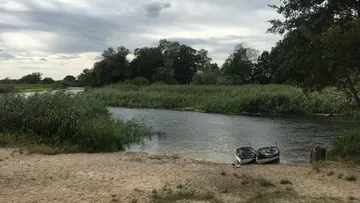 Zwei Kanus liegen am Ufer eines ruhigen Flusses, umgeben von Bäumen.