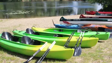 Grüne Kajaks liegen am Strand neben einem ruhigen Gewässer.