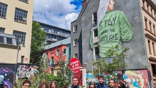 Gruppe steht vor einer Wandmalerei mit der Aufschrift „STAY WITH THE TROUBLE“.