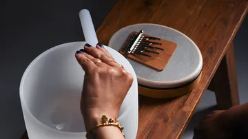 A hand holds a musical instrument next to a vessel.