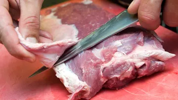 A piece of meat is cut with a knife, on a cutting board.