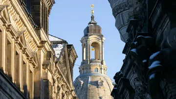 Church tower rises above historic buildings, blue sky.
