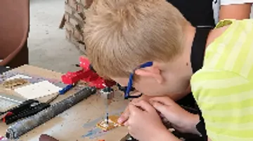Junge arbeitet konzentriert an einem Bastelprojekt am Tisch.