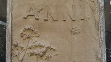 Gegossenes Sandrelief mit dem Namen `ANNY` und Pflanzenmotiven.