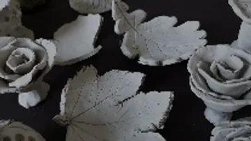 Blätter und Rosen aus weißem Material liegen auf schwarzem Hintergrund.