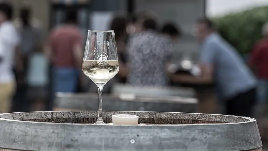 Wine glass stands on a wooden barrel, people in the background.