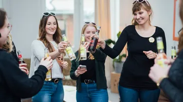 Flaschen werden bei einer Feier angestoßen, fröhliche Frauen.