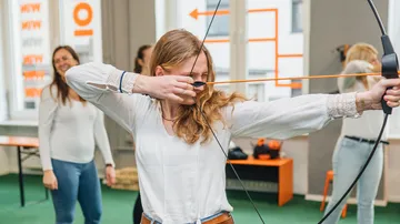Junge Frau zielt mit Bogen in einem Trainingsraum.