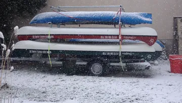 Three boats are parked on a trailer in the snow.