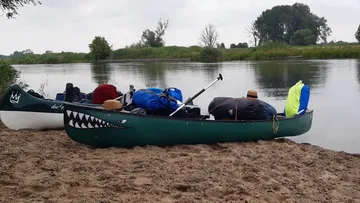 Two canoes lie on the sandy shores of a calm body of water.