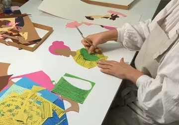 A person cuts colorful paper figures on a table.