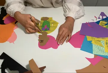 Hände schneiden farbige Papiere auf einem Tisch.