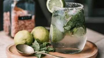 Ein Cocktailglas mit Minze und Limette auf einem Tablett.