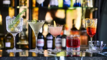 There are five cocktails on a bar with drinks in the background.
