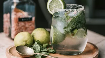 Cocktail glass with lime and mint on wooden plate.